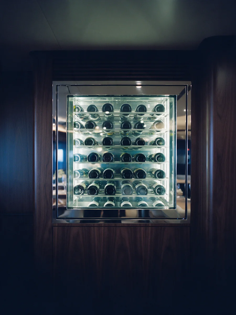 A glass-fronted wine cellar set into dark walnut panelling aboard a yacht